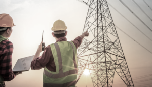 Two engineers with a laptop looking at an electricity pylon